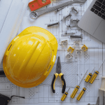 Desk with construction tools, hard hat, and laptop for T5018 filing preparation