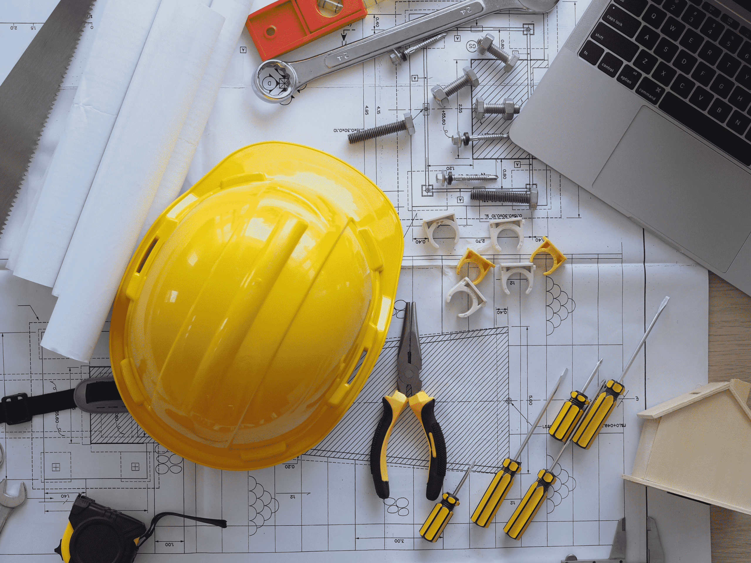 Desk with construction tools, hard hat, and laptop for T5018 filing preparation